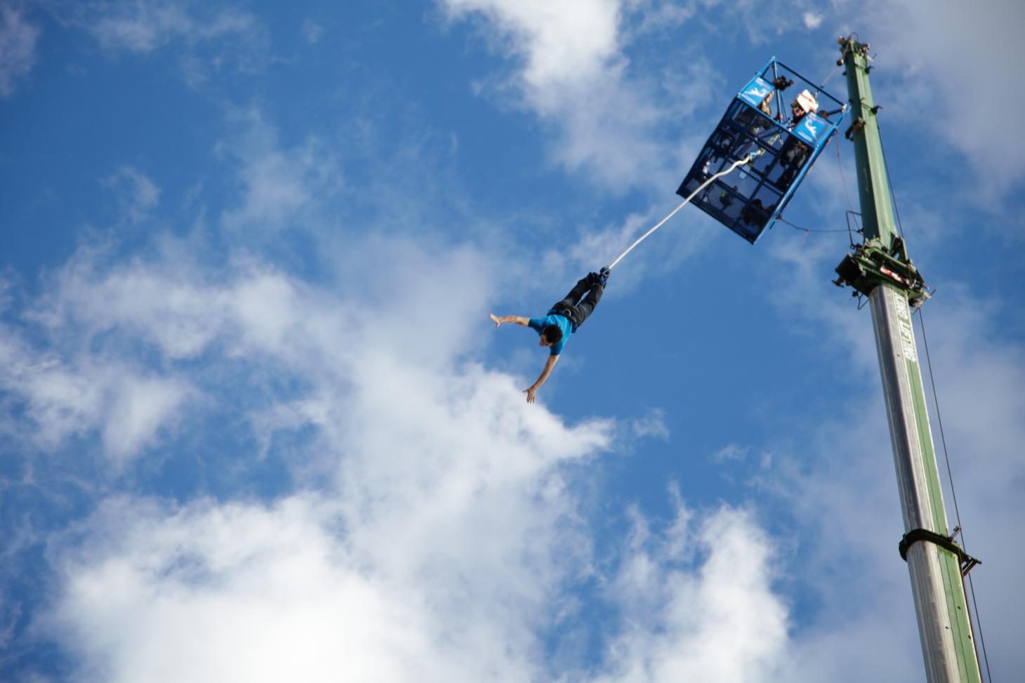 person bungee jumping against blue sky backdrop with white clouds