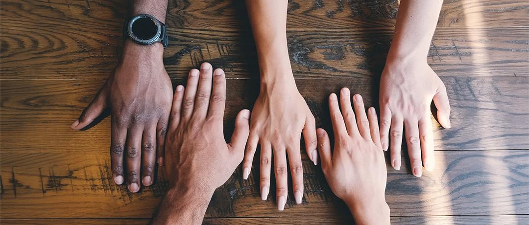 Five human hands on brown wooden surface